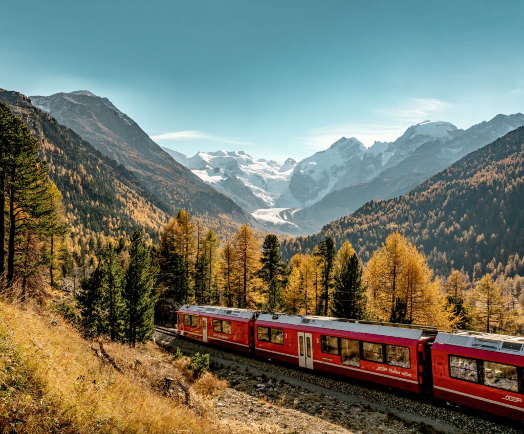 A red train passing through an autumnal Alpine landscape