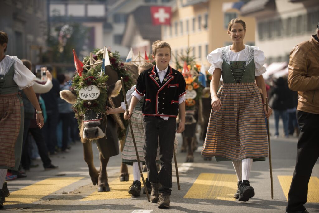 A child and a woman dressed in traditional regalia lead a herd of decorated cows through the centre of a Swiss town