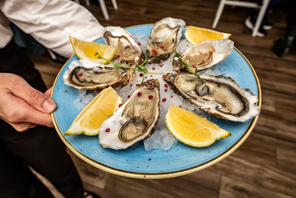 A bue plate with yellow lemon quarters and six open oysters.