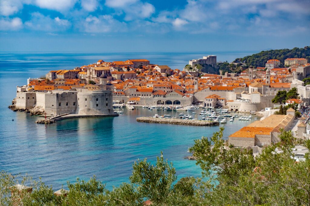 Organge roofs and pale grey brick houses in the medieval walled city of Dubrovnik jut out in a bright blue sea