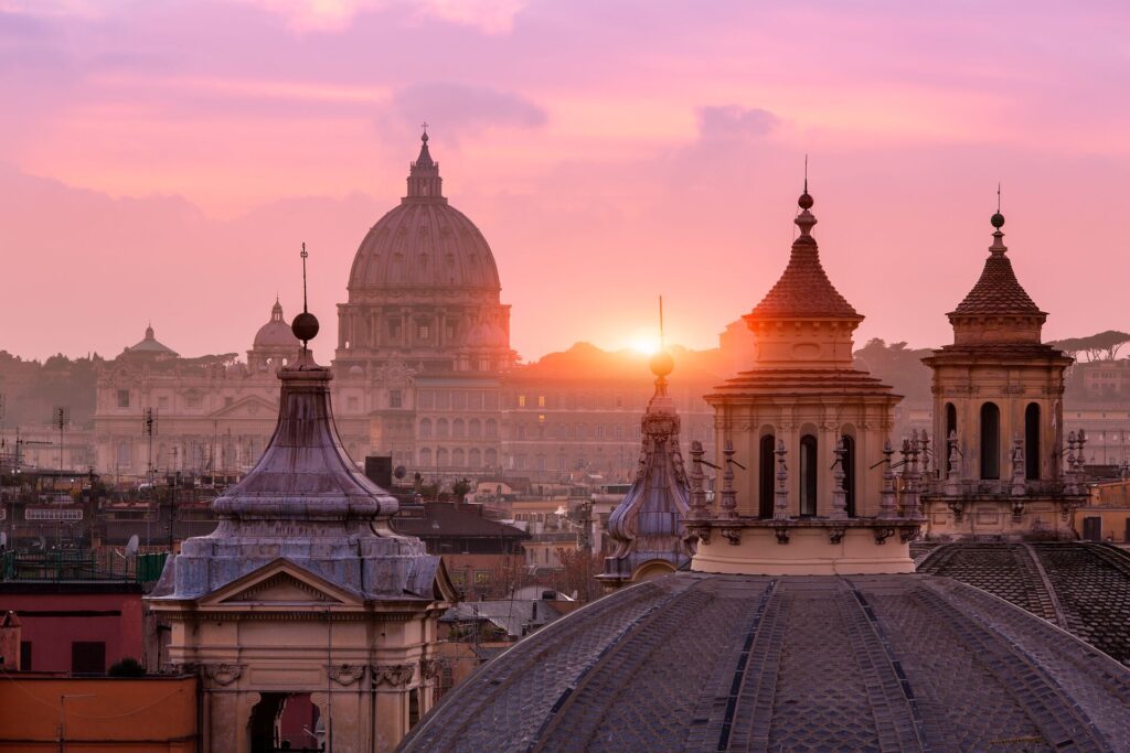 St Peter's Basilica in Rome, site of the Jubilee 2025, at sunset with a dramatic pink sky and the sun setting behind