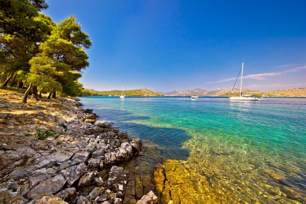 A low shot of clear green and blue sea with a white boat and a riocky shoreline