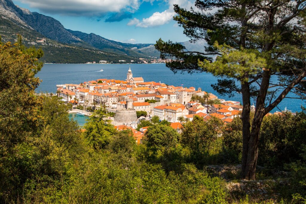 Aerial shot of red roofs and white buildings in the town of Korcula, Croatia with bright blue sea and sky.