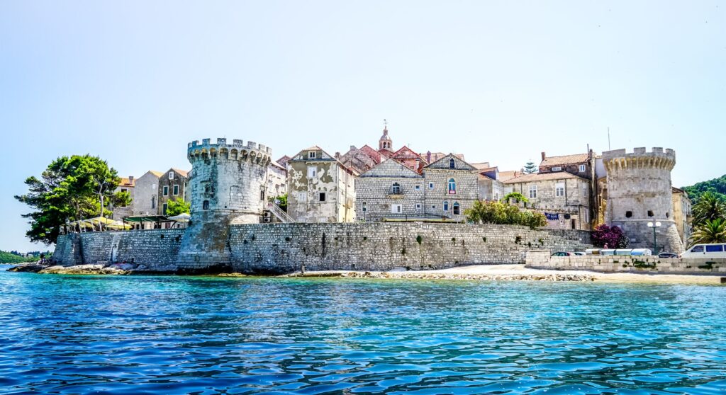 An ancient walled castle sits beside the bright blue sea in Korčula, Croatia.