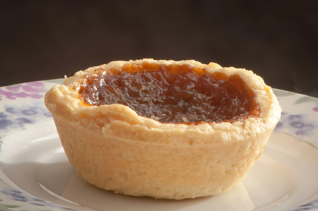 A close up of a small pastry tart with an orangey, jam like filling, on a china plate.