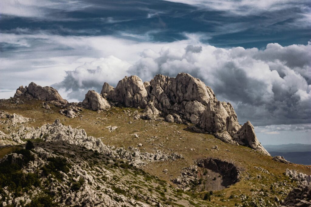 Craggy mountains with rick formations, with billowing clouds and a dramatic grey sky in the background. 