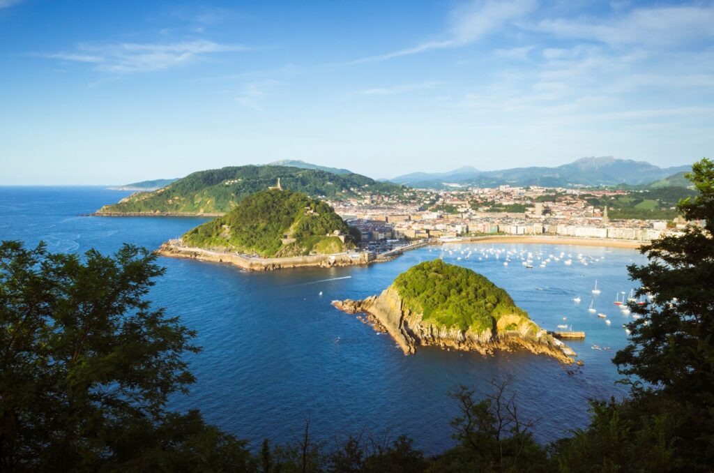 Aerial view of blue sea, bright green islands and a seafront toen with a long sandy beach, in San Sebastian Spain