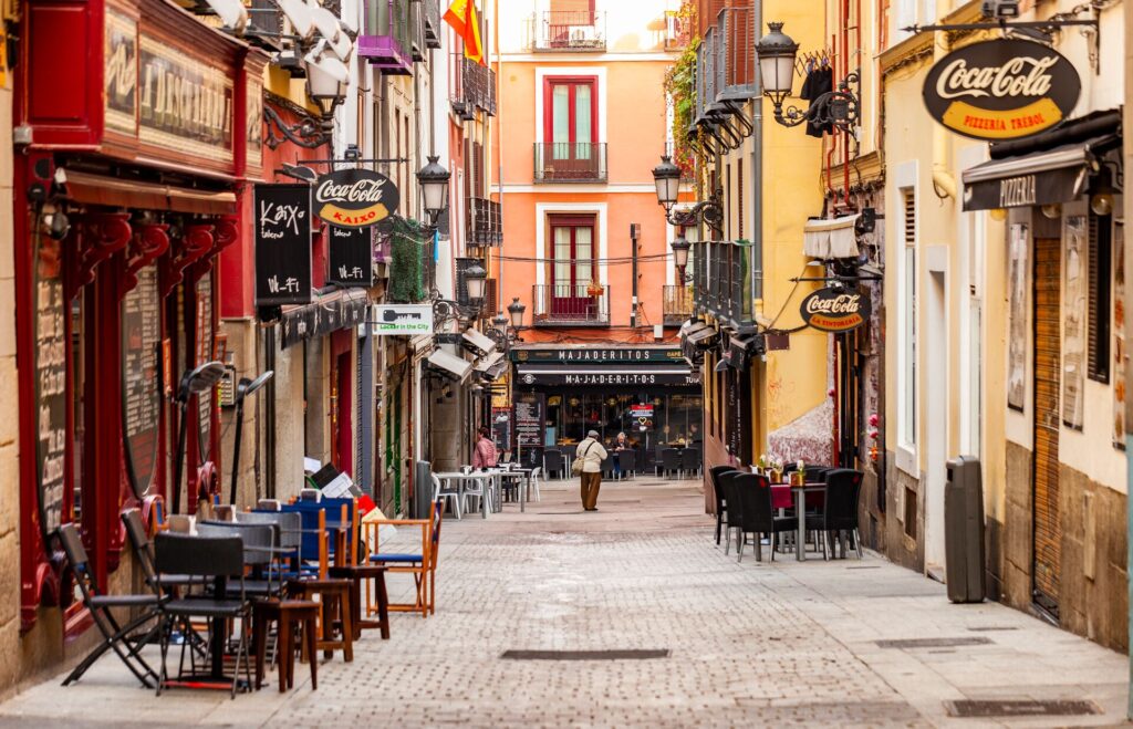 a cobbled street in Madrid, Spain with colorful old style shops, iron balconies, shop signs and chari outside a cafe