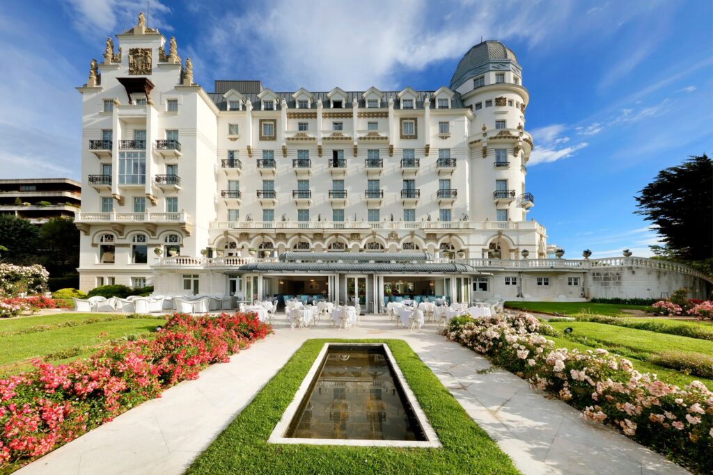 Grand white facade of the eurostar real hotel in Santander, Spain, with ornate gardens and colorful flowers in front