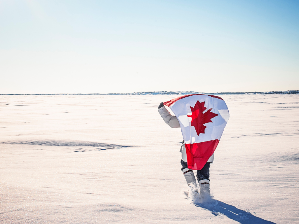 person holding canadian flag walking through tundra in the canadian arctic