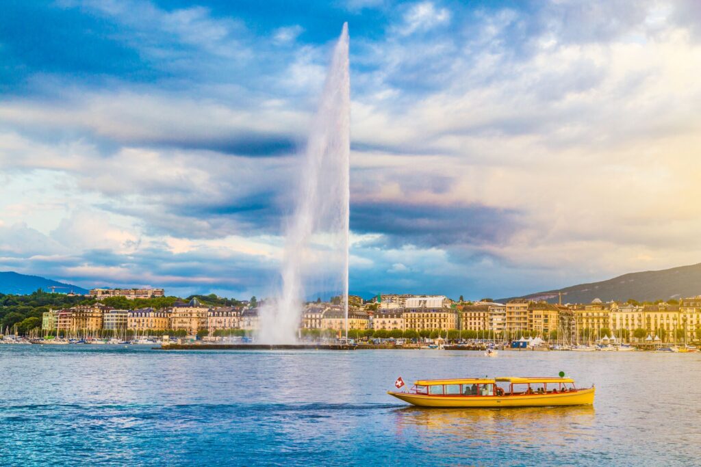 The water jet on Lake Geneva in Switzerland, with large buildings behind and a bright blue lake and bright blue sky.