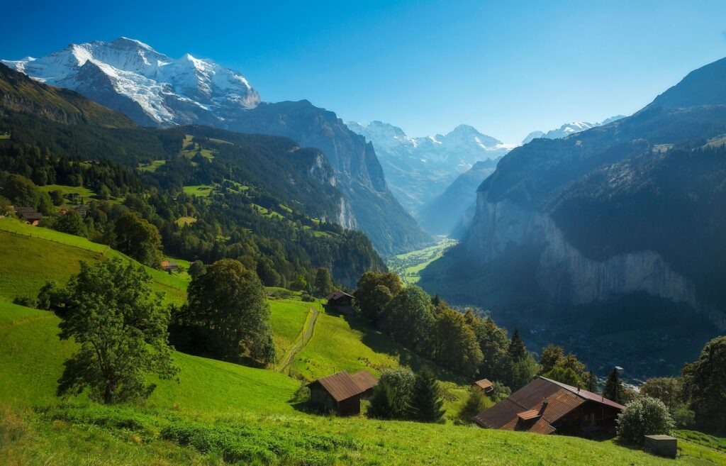 Green hills, with mountain huts and snow capped mountains in the background in Jungrfau region