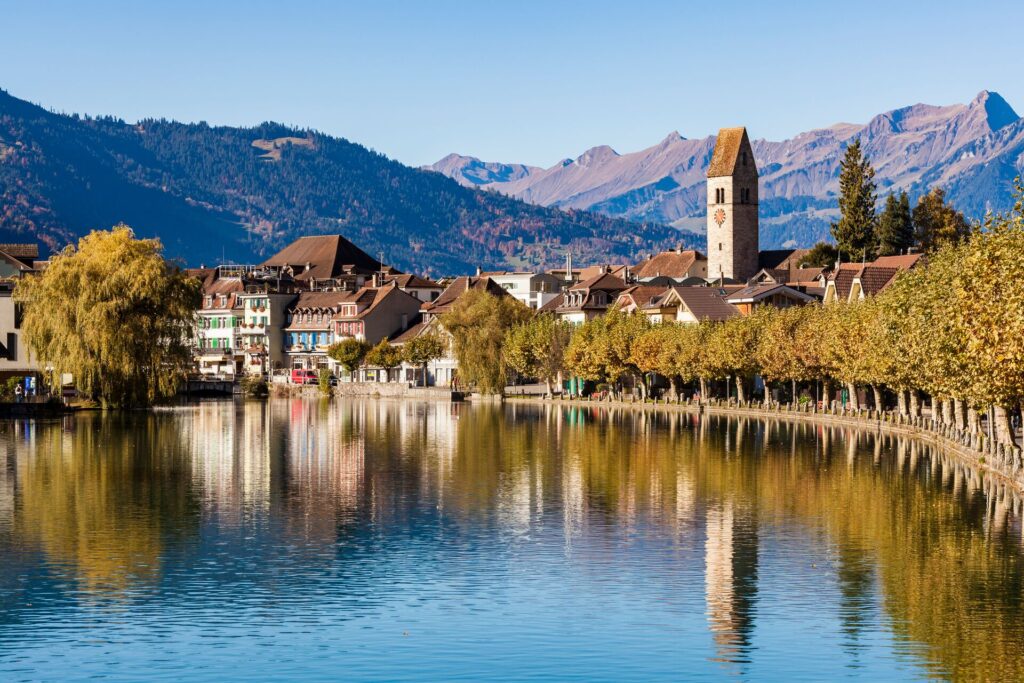 Medieval houses in Bern, Switzerland, flank the lakeside with mountains in the background