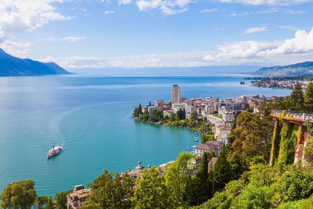 Vast, green waters of Lake Geneva in Switzerland,with blue sky. white clouds, and the city of Montreux tucked on the waters edge