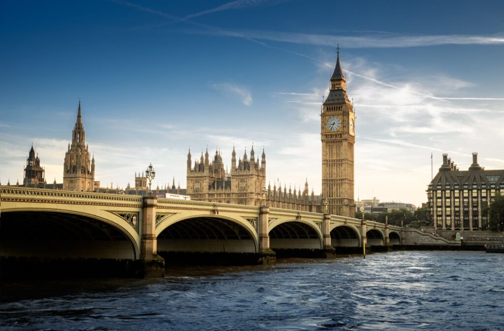 Big Ben and the Houses of Parliament glow golden in the sunlight, pictures behind a bridge and the River Thames