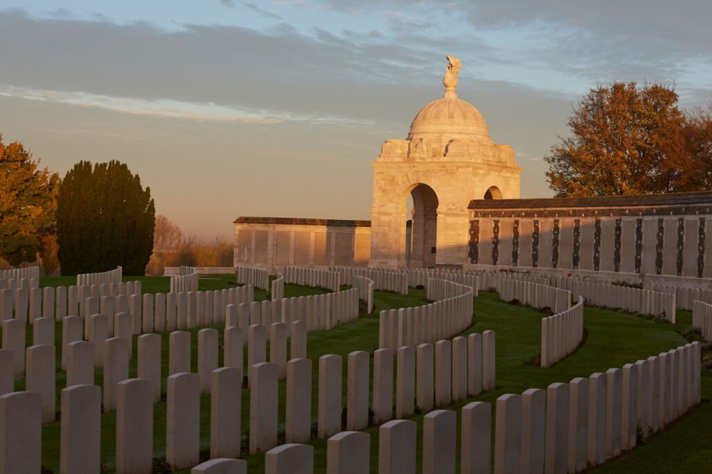 WWI memorial graveyard with semi circular rows of identical white gravestones and a large monument building behind.