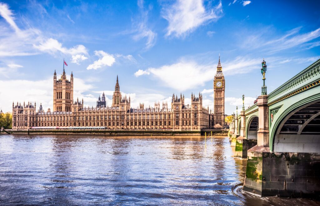 London's Big Ben clock and Houses of Parliament with the River Thames and a green bridge in front.