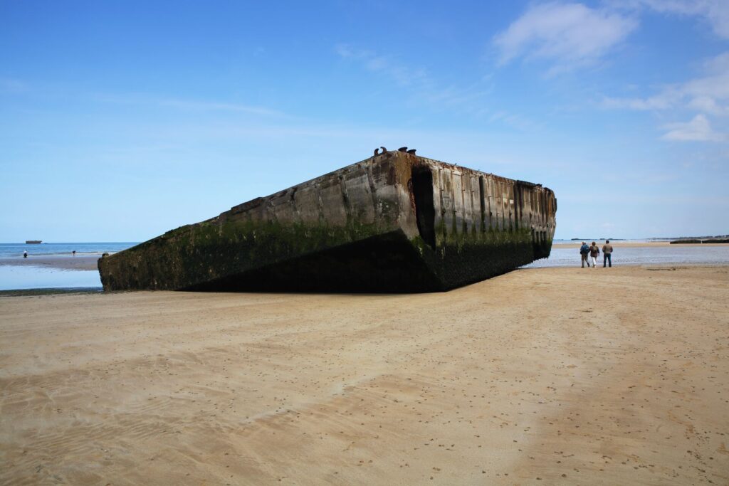 Close up shot of part of the Mulberry floating harbour lies on a stretch of sand with a bright blue sky on Normandy Beach in France.