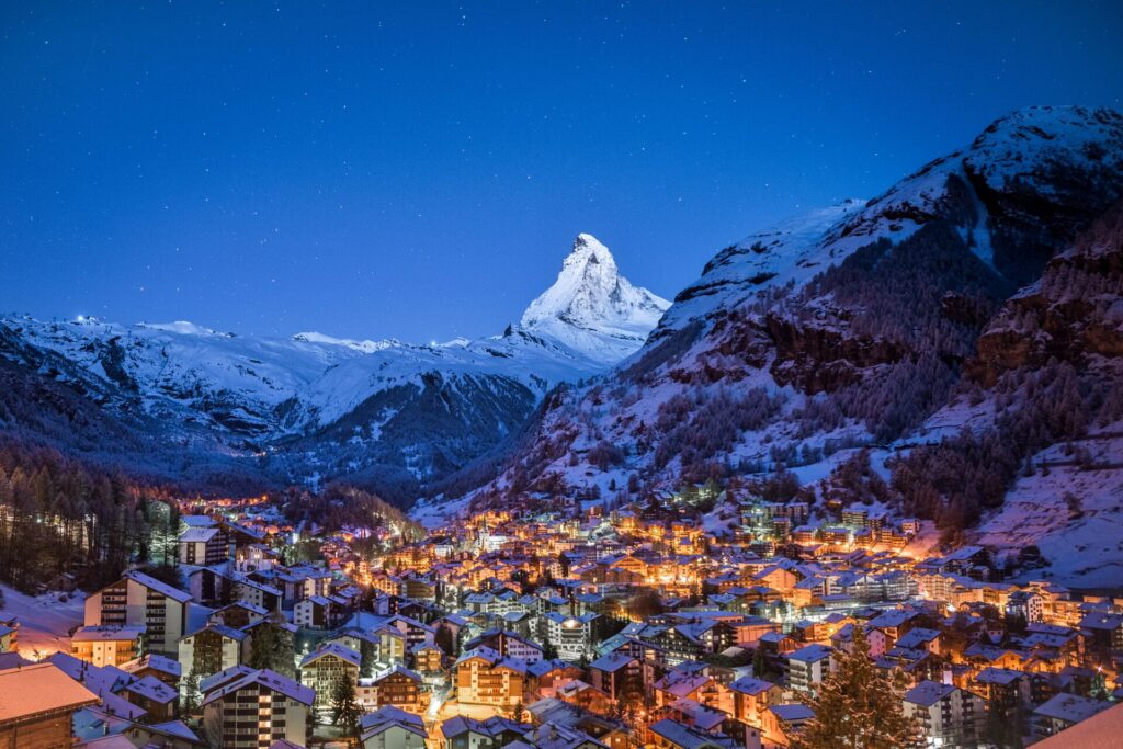 The Swiss town of St Moritz glistens with lights in the evening, with the snow capped Matterhorn mountain in the background.