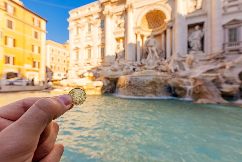 holding euro in front of trevi fountain