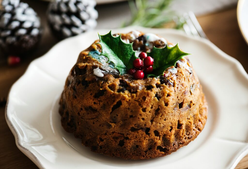 English Christmas Pudding on a white plate with holly and red berries on the top, part of a traditional English Christmas dinner.