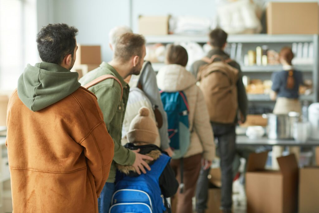 Five people stand in a queue in a shop, the epitome of UK manners, photographed from behind.