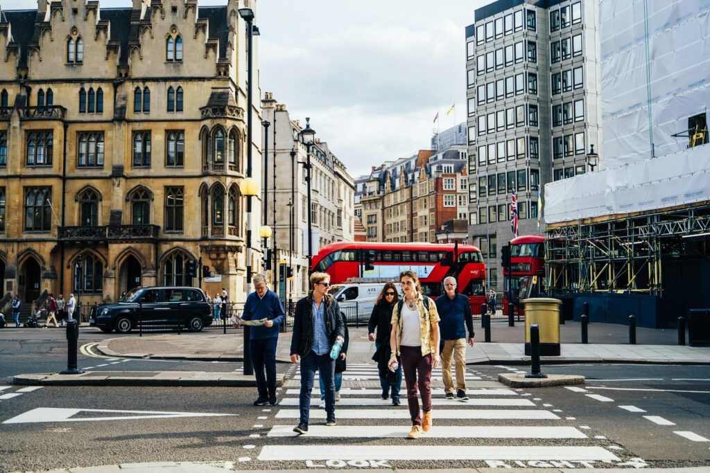 A group of people cross across a black and white zebra crossing with a red double decker bus behind in London, Britain.