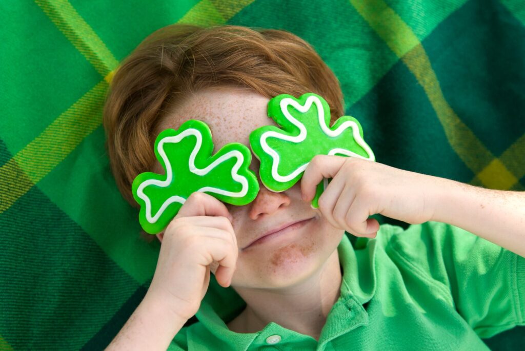 A child holing green shamrocks over his eyes