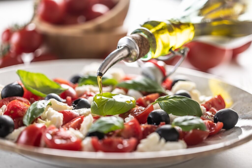 Olive oil is poured onto a plate of mozzarella cheese, tomatoes and olives in Italy